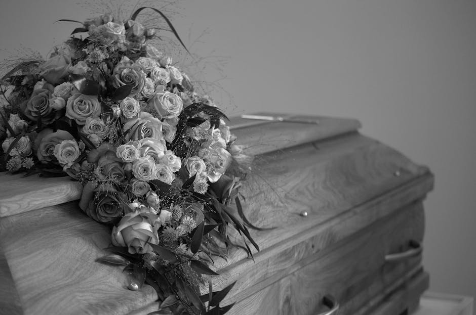 A large, elegant floral arrangement of fresh roses, carnations, and other flowers in various shades of white, cream, and light pink, intricately assembled into a bouquet with greenery and delicate fil