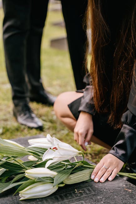 A person kneeling on the ground, arranging a bouquet of white lilies with long green leaves, likely for a floral tribute. The lilies, with their large, trumpet-shaped petals and prominent stamens, app