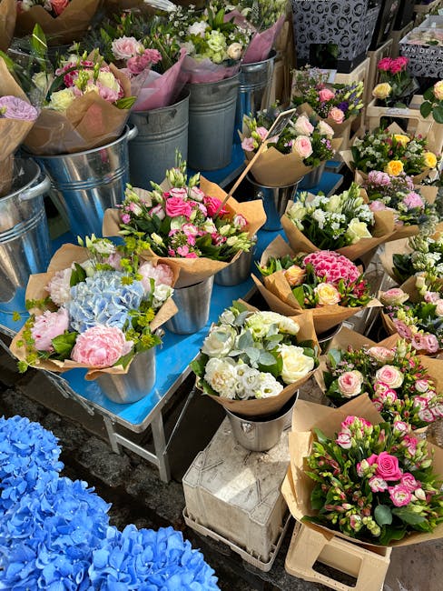 An array of freshly arranged floral bouquets and flower arrangements displayed on a table, featuring a variety of blooms including pink roses, white hydrangeas, pale pink peonies, and soft blue hydran