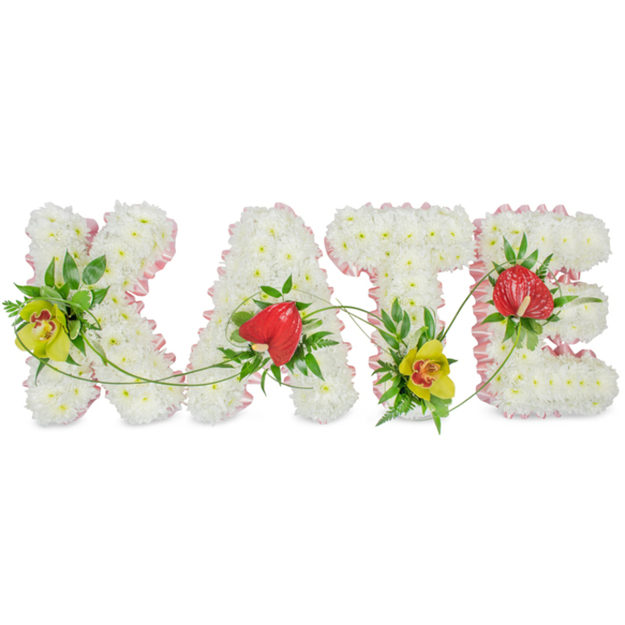 This image shows a carefully designed floral name tribute spelling out "KATE" in four large block letters, the kind of bespoke memorial arrangement frequently prepared by Florist South Wimbledon for families across the SW19 area. The letters stand out crisply against a bright white backdrop, allowing every petal and ribbon fold to be clearly seen. Each character is tightly massed with pure white chrysanthemums, creating a dense, cushion-like texture that conveys peace and innocence. Around the outside edge of every letter runs a slim border of light pink satin ribbon, gathered slightly so it forms gentle ruffles that soften the lines and introduce a touch of quiet femininity. Carefully placed amongst the white blooms are distinctive focal flowers. On the "K" and the "T", yellow-green cymbidium orchids with speckled, reddish-brown centres add an exotic note, their waxy petals and strong colour giving the tribute life and freshness. On the "A" and "E", glossy, heart-shaped red anthurium blossoms nestle among dark green leaves, their deep crimson hue symbolising love, respect, and remembrance. Threading through the entire design, fine tendrils and trails of green foliage curve and weave from one letter to the next, visually linking K to A, A to T, and T to E, as if binding the name together with a ribbon of living green. The tribute feels both personal and dignified, ideal for a funeral, cremation service, or celebration of life at a local South Wimbledon chapel, providing a tender, unmistakably individual way to remember someone called Kate with flowers that speak softly yet clearly of love and farewell.