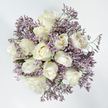 Viewed from directly above, this bouquet appears as a perfectly rounded pool of calm light, its flowers arranged in a neat, circular cluster against a clean, radiant white backdrop that gives the design an almost weightless quality. At the heart of the arrangement sit around a dozen white roses, their petals thick, velvety, and luxuriously layered. Some blooms remain in tight, protective buds, while others loosen into soft spirals, and a few stand fully open, revealing intricate centres that invite the eye to linger. The colour of the roses is a sophisticated cream, brushed with faint ivory and the gentlest trace of pale buttery yellow at the base of the petals, offering a sense of warmth and humanity that pure white alone might lack. Encircling and weaving between these roses are airy sprays of lavender Limonium, thousands of tiny, papery blossoms gathered on slender stems to form a delicate purple halo. The limonium's lilac tone is understated and soothing, a quiet echo of the soft blooms and spring shades you might see along the edges of South Wimbledon's residential streets or in small local gardens. Fine green stems and minimal foliage appear only intermittently, just enough to anchor the composition without disturbing its restrained elegance. The bouquet feels thoughtfully and lovingly composed, as though arranged by a South Wimbledon florist accustomed to creating tributes for funerals, remembrance services, and sympathy deliveries across nearby neighbourhoods. It conveys a mood of peace, consolation, and respectful tenderness, ideal for moments when a gentle floral gesture needs to carry emotions that are difficult to express aloud.